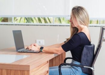 Mulher sentada na frente do computador com almofada lombar